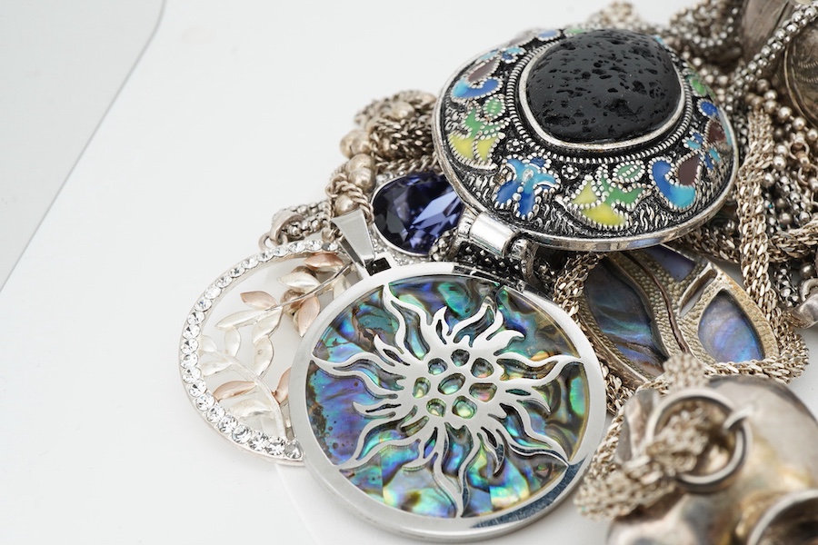 A collection of silver and costume jewellery, comprising: a pendant designed as an elephant; an enamel and porous black stone pendant; five shell medallion pendants; two paste pendants; and a treated amber pendant; all w